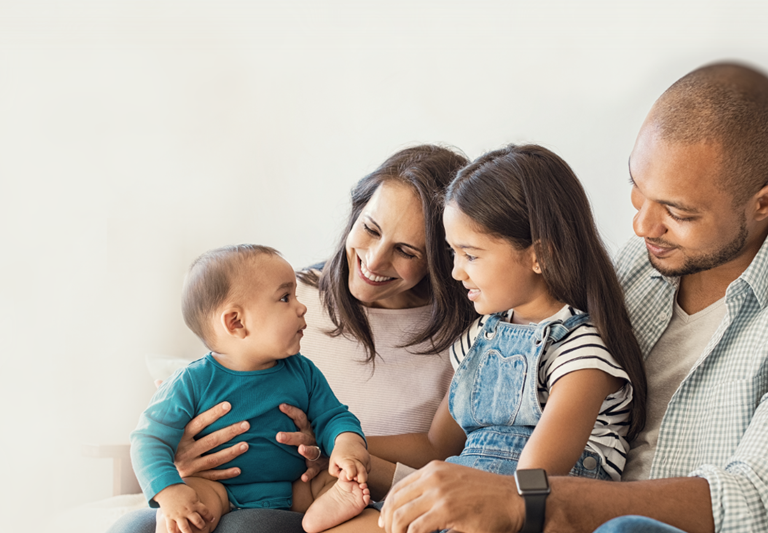 Familia multiétnica. Niña sentada en la pierna de papá y mirando a su nuevo hermano lindo sentado en el regazo de mamá.