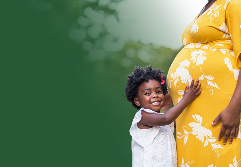 Mujer embarazada afroamericana con su hija pequeña abrazando su vientre.