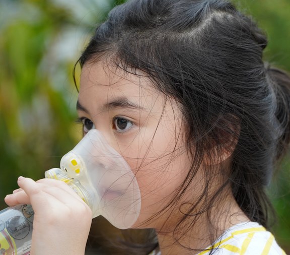 Niña asiática con asma usando inhalador y espaciador. Sistema respiratorio y alergias.