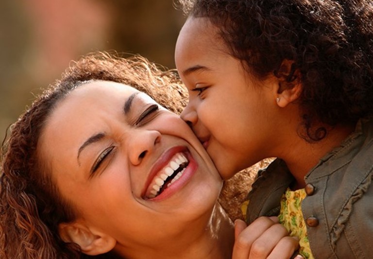 Mamá afroamericana siendo besada en el cheque por su hija