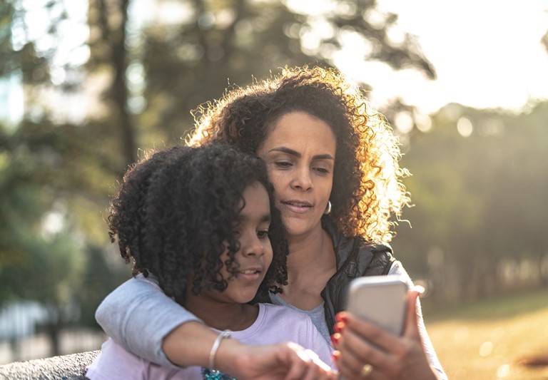 Mamá afroamericana mirando el teléfono celular con su hija.