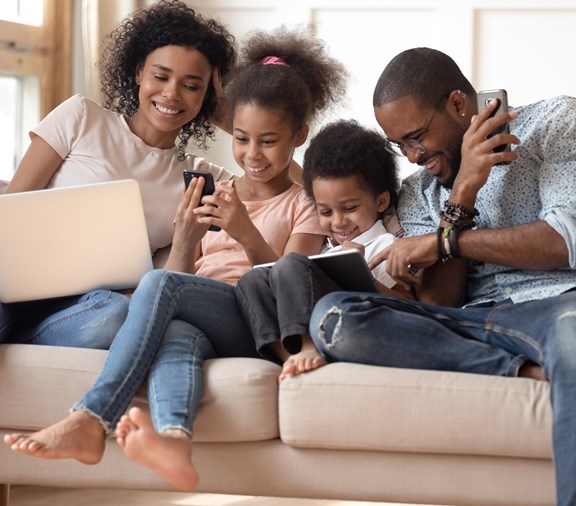 Familia feliz sentada en el sofá juntos usando diferentes dispositivos tecnológicos