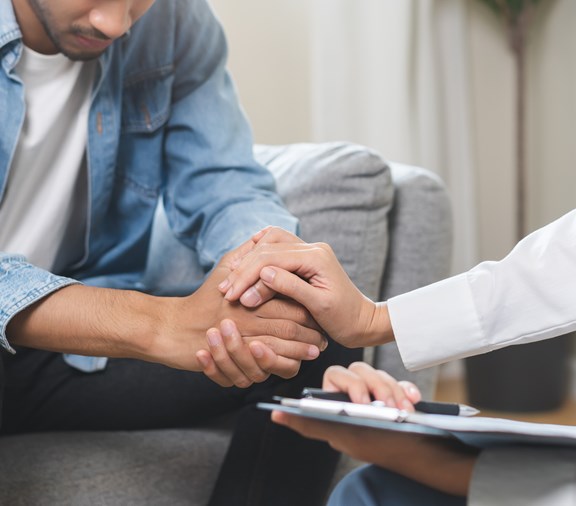 Salud conductual, depresión. Un joven triste consulta con un psiquiatra mientras un paciente recibe terapia psicológica con un médico en la clínica. El médico anima a una persona con problemas de salud mental.